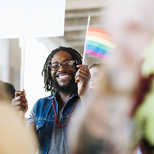 Black man holding a pride flag smiling at the camera